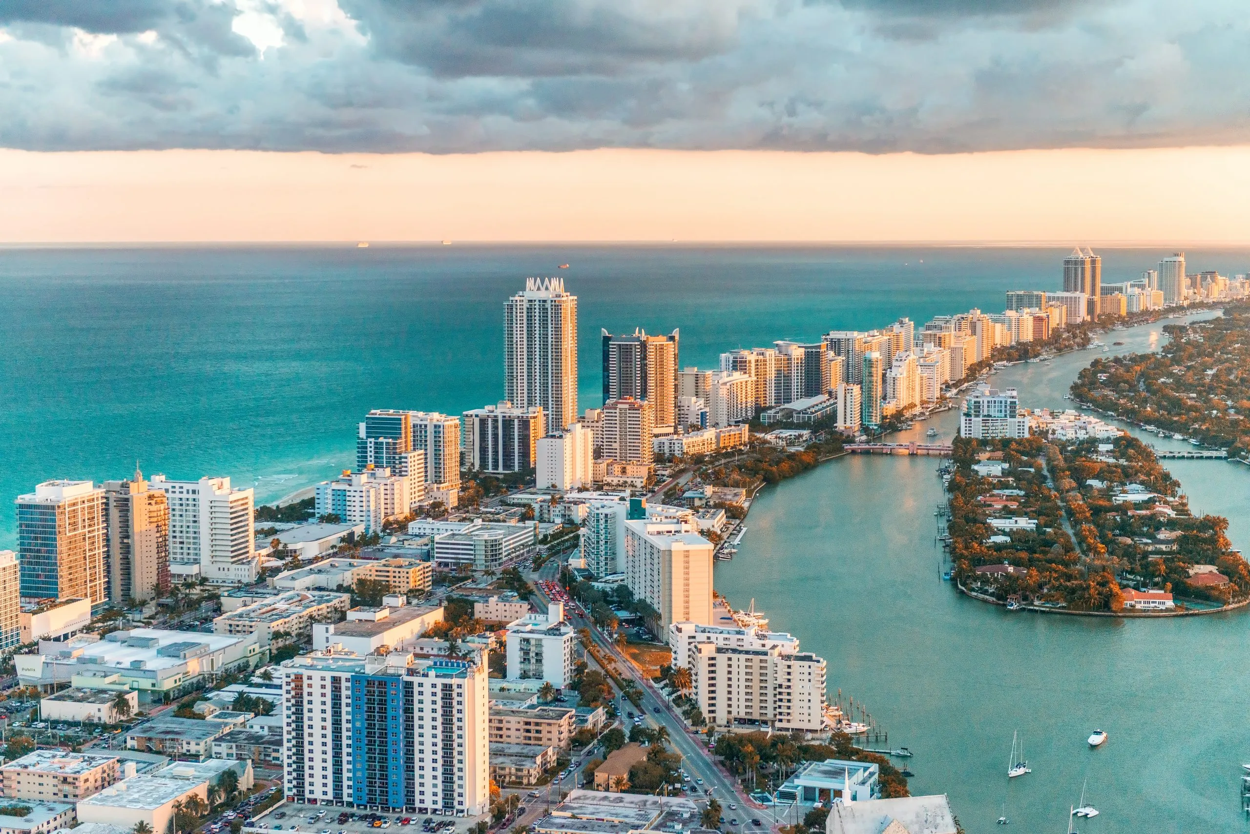 Aerial view of Miami Beach skyline at sunset, oceanfront high-rises, Intracoastal Waterway with boats.