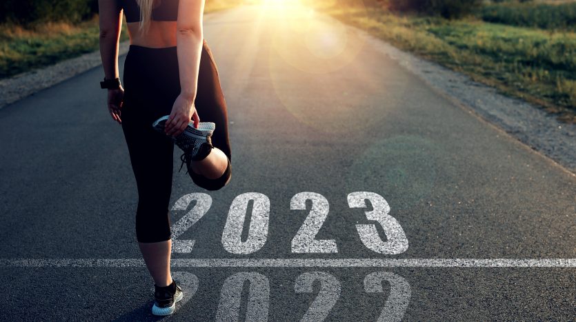 A female runner stretches while standing at the 2023 starting line and 2022 finish line